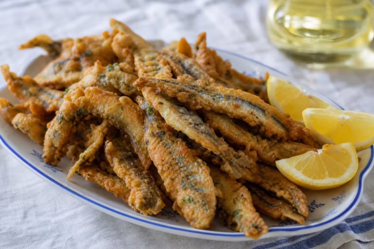 Anchois frits dorés servis sur un plat en faience ancienne avec citron