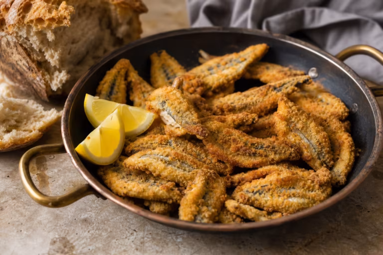 Anchois panés croustillants dans une poêle en cuivre avec quartiers de citron