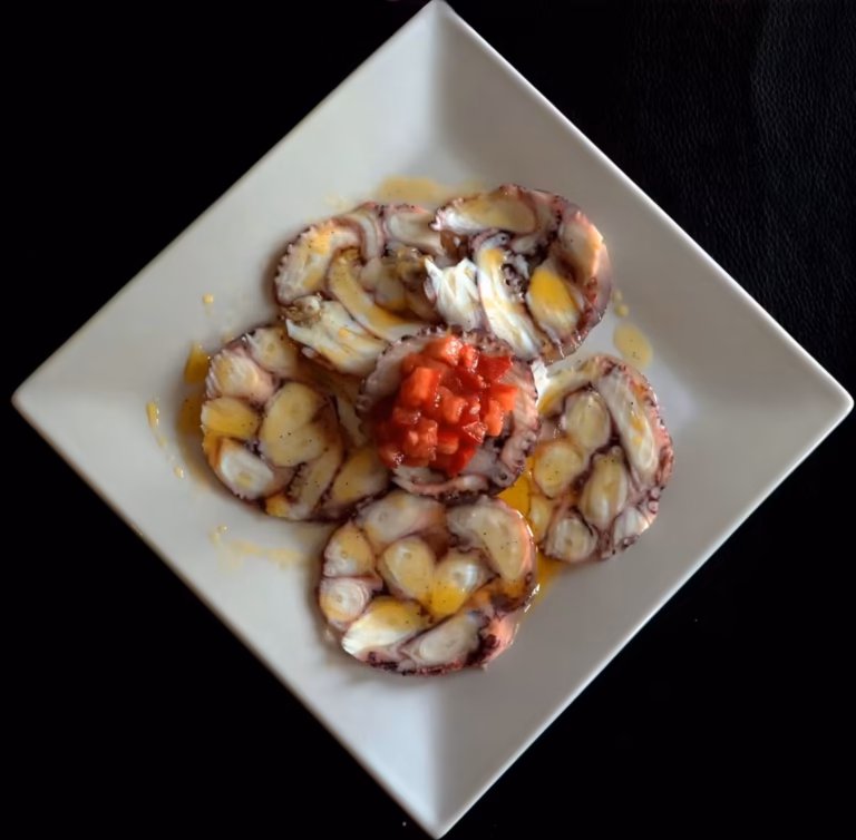 Carpaccio de poulpe en rosaces sur une assiette carrée, brunoise de tomates au centre