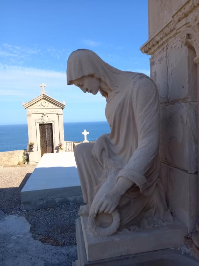 Statue de pleureuse tenant une couronne au cimetière marin de Sète, devant une chapelle funéraire et la mer