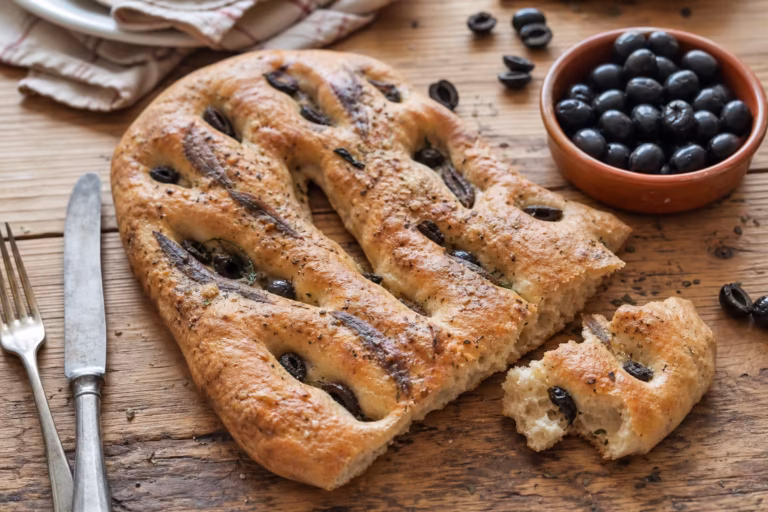 Fougasse aux olives noires et anchois dorée sur table en pin brut