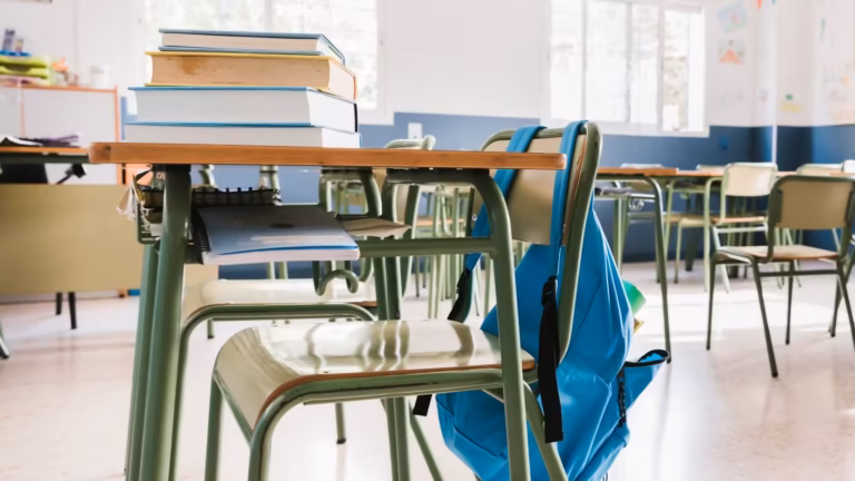 Salle de classe vide avec livres sur un pupitre et cartable accroché à une chaise