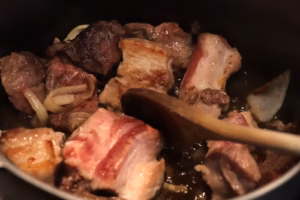 Poitrine de porc et bœuf en train de dorer avec l'oignon pour la macaronade