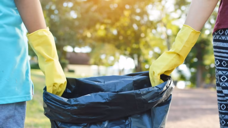 Deux bénévoles gantés tiennent un sac poubelle lors d'un ramassage de déchets en plein air