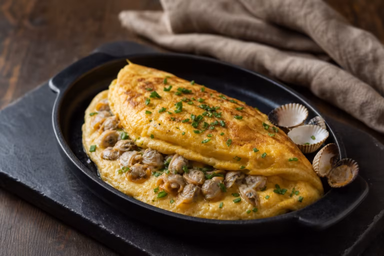 Omelette baveuse aux coques décoquillées, persil et ciboulette dans un plat en fonte