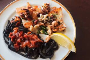 Seiches dorées au chorizo et pâtes à l'encre nappées de sauce tomate dans l'assiette