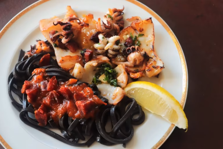 Seiches dorées au chorizo et pâtes à l'encre nappées de sauce tomate dans l'assiette