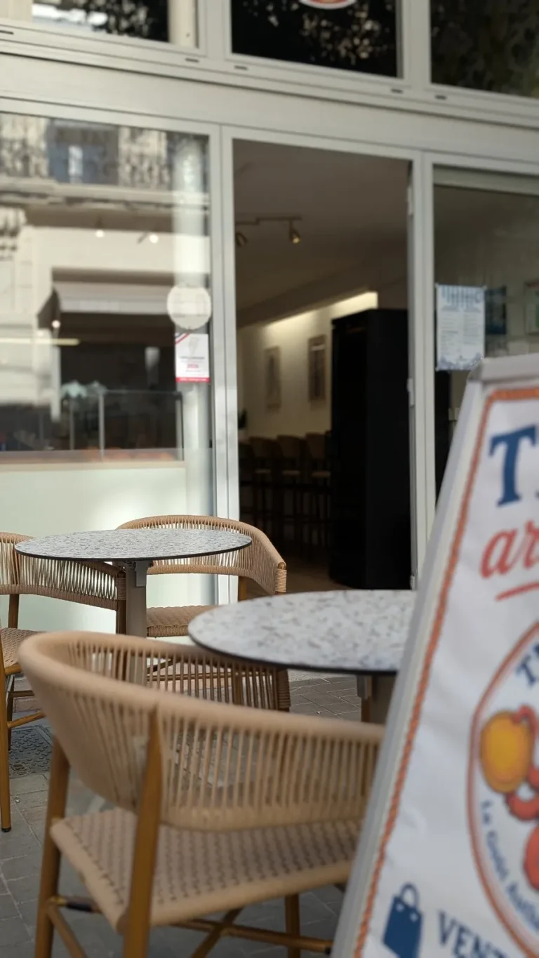 Terrasse avec tables en terrazzo et chevalet devant l'entrée de la tiellerie
