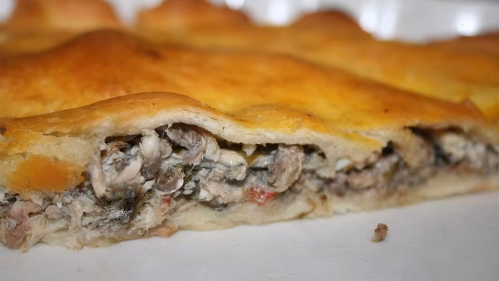 Tielle aux anchois cuite, tranchée, montrant la garniture dorée