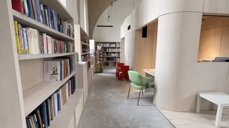 Allée de la nouvelle bibliothèque de la MJC de Poussan, avec rayonnages en bois clair, voûte en pierre et chaises rouges d'enfants