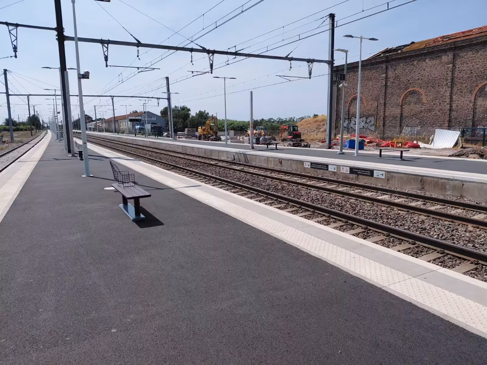 Quai de la gare d'Agde avec des bancs, et des engins de chantier en arrière-plan