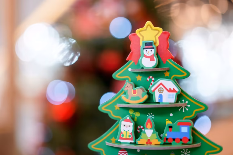 Petit sapin de Noël en bois décoré de figurines colorées, bonhomme de neige, cheval à bascule et père Noël, devant des lumières floues