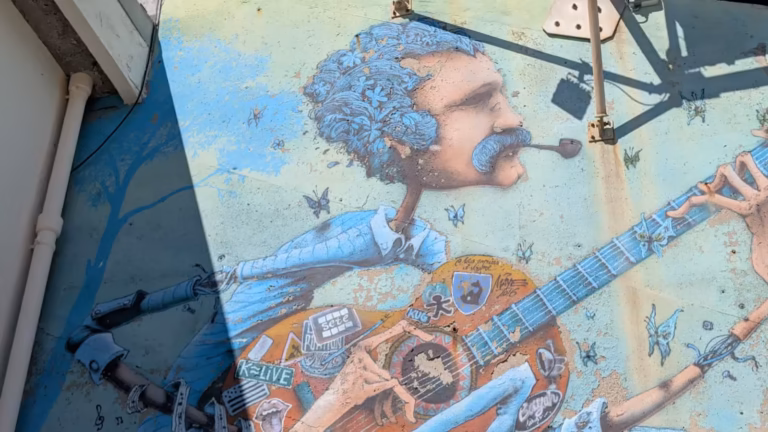 Fresque murale d'un musicien à la guitare, détail du visage et de l'instrument, au Théâtre de la Mer à Sète