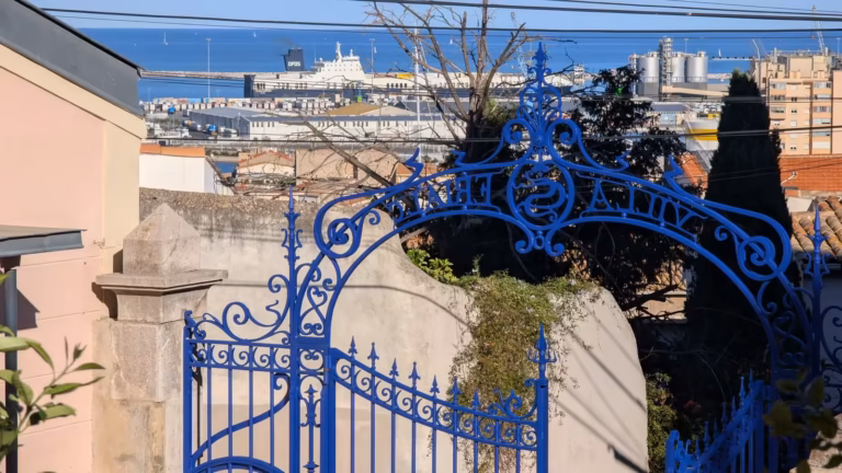 Portail en fer forgé bleu de l'école des Beaux-Arts de Sète, avec le port de Sète en arrière-plan