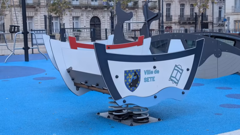 Jeu à ressort en forme de barque aux armes de la Ville de Sète, avec le toboggan en forme de baleine derrière, sur la place Aristide Briand