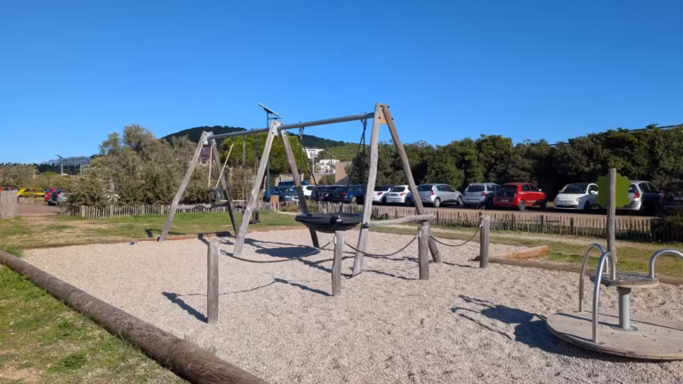 Balançoires et jeux de l'aire, voitures stationnées en fond