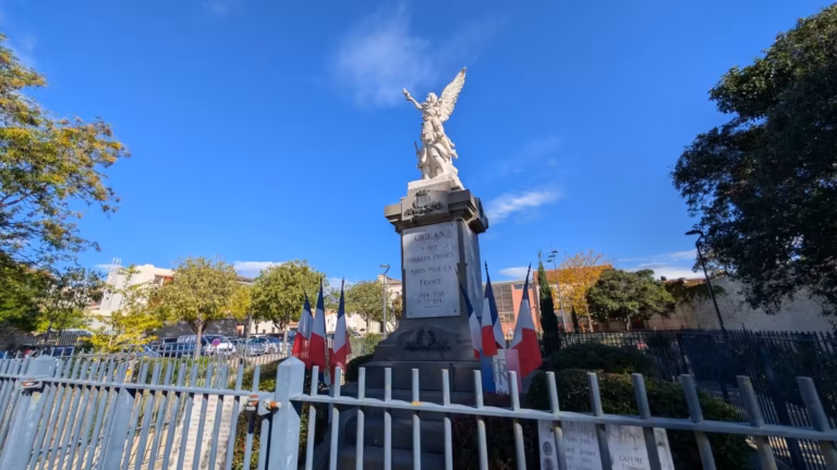 Monument aux morts de Gigean et ses drapeaux derrière la grille