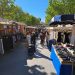 Allée d'un marché en plein air à Mèze, étals de vêtements sous les arbres