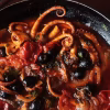 Poulpe de roche mijoté aux tomates cerises, olives noires et persil dans une poêle en fonte